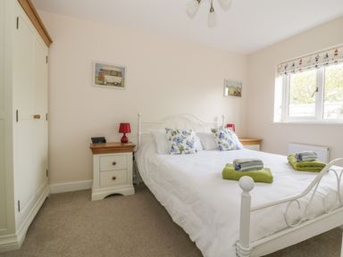 A bedroom with a white metal bed frame two bedside cabinets with lamps and a wardrobe at Sandlings in Hollesley near Woodbridge