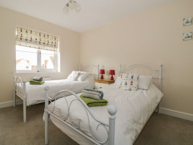 A bedroom with two beds with white frames and bedding a window with patterned blinds and a bedside table with two red lamps at Sandlings in Hollesley near Woodbridge