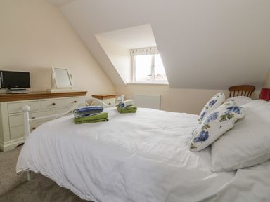A bedroom with a bed white bedding floral pillows folded towels dressers and a window at Sandlings Hollesley near Woodbridge