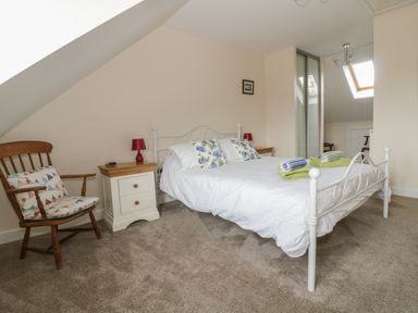 A bedroom with a white metal bed with floral pillows two bedside tables with red lamps a wooden chair with cushions and a skylight window at Sandlings in Hollesley near Woodbridge