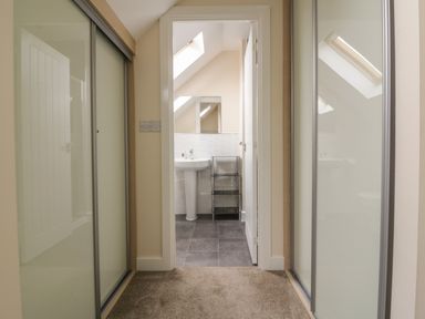A hallway with carpet and sliding closet doors leading to a bathroom with a pedestal sink and tiled floor at Sandlings in Hollesley near Woodbridge