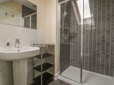 A bathroom with a sink pedestal a small shelving unit and a shower with dark tile walls at Sandlings in Hollesley near Woodbridge