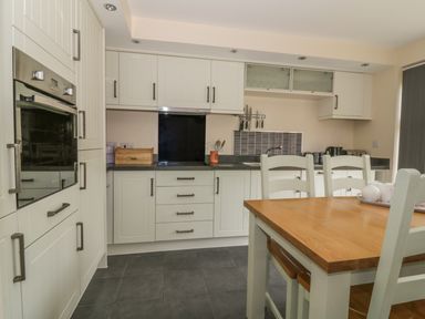 A kitchen with white cabinets a wooden dining table and chairs at Sandlings in Hollesley near Woodbridge