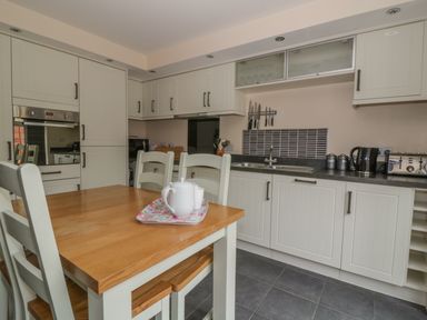 A kitchen with white cabinets a wooden dining table and chairs a kettle toaster and knives on a magnetic strip at Sandlings in Hollesley near Woodbridge