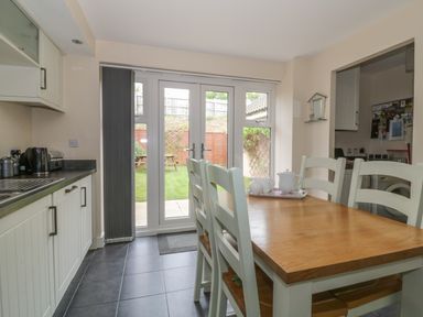 A kitchen with a wooden dining table and chairs and white cabinets near glass doors leading to a garden at Sandlings Hollesley near Woodbridge