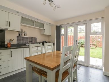 A kitchen with a wooden dining table and white chairs near glass doors opening to a garden at Sandlings in Hollesley near Woodbridge