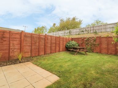 A backyard garden with grass a wooden picnic table and fenced boundaries at Sandlings in Hollesley near Woodbridge