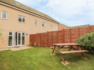 A backyard with a wooden picnic table on grass and a fenced garden at Sandlings in Hollesley near Woodbridge