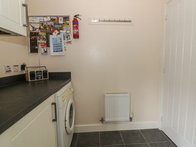 A laundry room with a washing machine countertop a radio fire extinguisher and a coat rack at Sandlings in Hollesley near Woodbridge