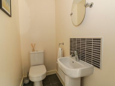 A bathroom with a toilet a sink a round mirror and a wall-mounted towel ring at Sandlings Hollesley near Woodbridge