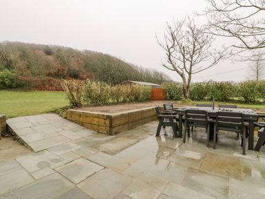 An outdoor patio with a dining table and chairs near a raised garden bed and trees at Gwelfor in Morfa Bychan