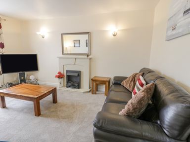 A living room with a leather sofa a wooden coffee table a TV on a stand and a fireplace at Gwelfor in Morfa Bychan