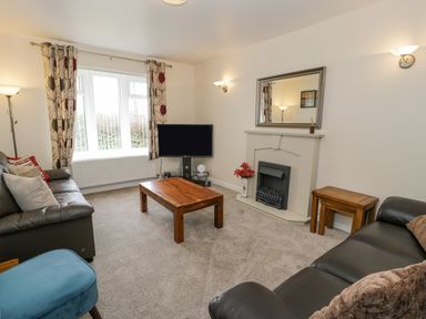 A living room with two black leather sofas a wooden coffee table a TV on a stand and a fireplace with a mirror above at Gwelfor in Morfa Bychan