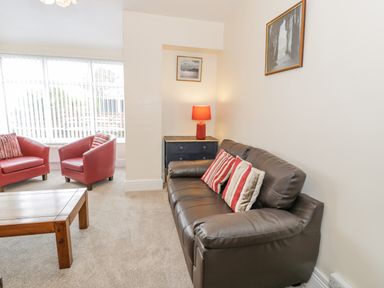 A living room with a brown leather sofa with striped cushions a wooden coffee table two red armchairs a black chest of drawers with a red lamp and framed pictures on the walls at Gwelfor in Morfa Bychan