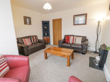 A living room with two brown sofas a red armchair a wooden coffee table and a fireplace at Gwelfor in Morfa Bychan