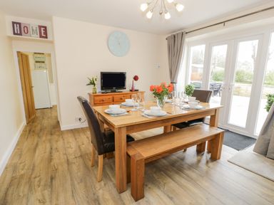 A dining room with a wooden table set for six with chairs and a bench and a TV on a wooden dresser at Gwelfor in Morfa Bychan