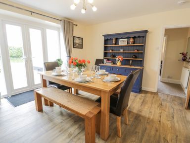 A dining room with a wooden table set for six with flowers and a blue cupboard against the wall at Gwelfor in Morfa Bychan