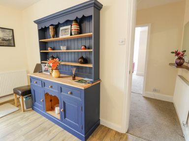 A blue wooden cabinet with shelves holding decorative vases and flowers next to a chair and a hallway at Gwelfor in Morfa Bychan
