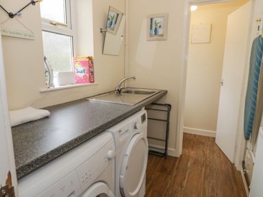 A utility room with a countertop sink washing machine dryer and ironing board at Gwelfor in Morfa Bychan
