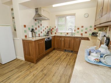 A kitchen with wooden cabinets a stove a sink a refrigerator and a tray with teapot and cups at Gwelfor in Morfa Bychan
