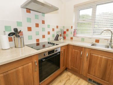 A kitchen with wooden cabinets an electric stove a stainless steel oven a sink and a window with blinds at Gwelfor in Morfa Bychan