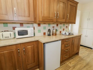 A kitchen countertop with wooden cabinets a toaster microwave kettle and a tray with a teapot and cups at Gwelfor in Morfa Bychan