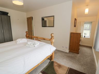 A bedroom with a wooden bed, folded towels on the bed, a dark wardrobe, a wooden chest of drawers, a mirror on the wall, and a window with curtains at Gwelfor in Morfa Bychan