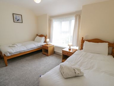 A bedroom with two single beds wooden nightstands and lamps by a window at Gwelfor Morfa Bychan