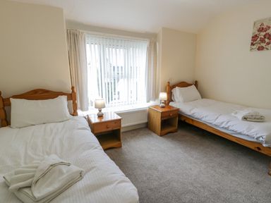 A bedroom with two single beds bedside tables lamps and a window at Gwelfor in Morfa Bychan