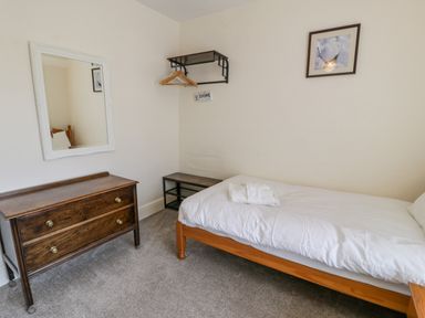 A small bedroom with a single bed wooden dresser mirror and wall shelf with hangers at Gwelfor in Morfa Bychan