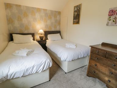 A bedroom with two single beds a nightstand with a lamp and a wooden dresser at Gwelfor in Morfa Bychan