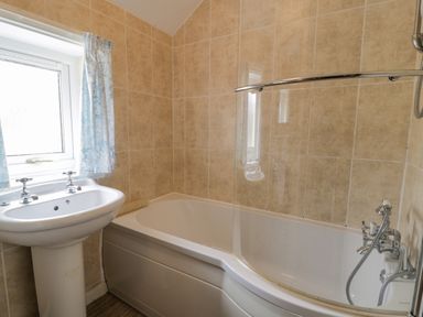 A bathroom with a bathtub a pedestal sink and a window with curtains at Gwelfor in Morfa Bychan