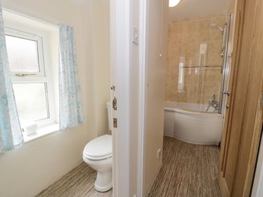 A bathroom with a toilet near a window with curtains and a bathtub with a shower at Gwelfor in Morfa Bychan