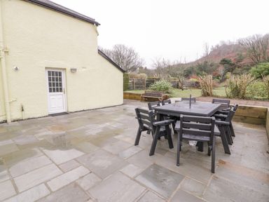 An outdoor patio with stone flooring black outdoor table and chairs and a bench near a fenced garden at Gwelfor in Morfa Bychan