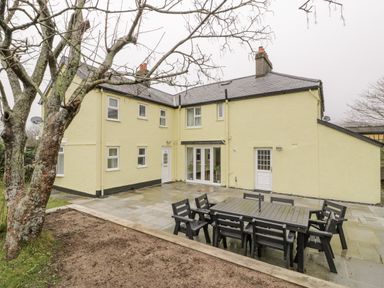 A backyard patio area with black outdoor dining furniture and a yellow two-story house in the background at Gwelfor in Morfa Bychan
