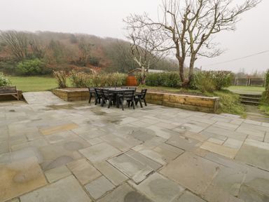 An outdoor patio with a black table and chairs surrounded by trees and greenery at Gwelfor in Morfa Bychan