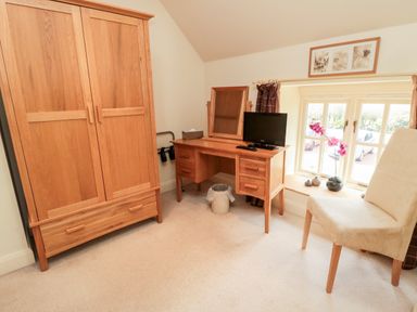 A bedroom with a wooden wardrobe dressing table a chair and a window at The Granary in Longframlington near Alnwick