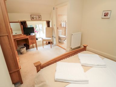 A bedroom with a wooden bed, desk with a mirror and television, chair, and a bathroom visible at The Granary in Longframlington near Alnwick