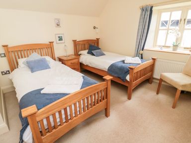 A bedroom with two single wooden beds bedside table a chair and a window with curtains at The Granary in Longframlington near Alnwick