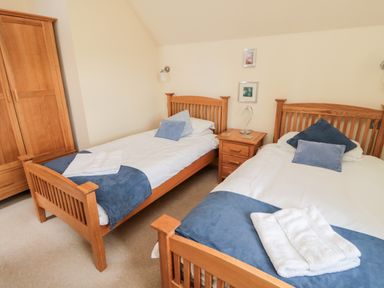 A bedroom with two single wooden beds bedside table and wardrobe at The Granary in Longframlington near Alnwick