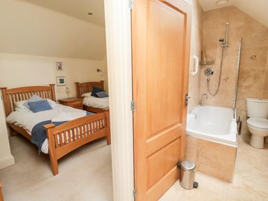 A bedroom with two wooden single beds and a nightstand next to a bathroom with a bathtub and toilet at The Granary in Longframlington near Alnwick