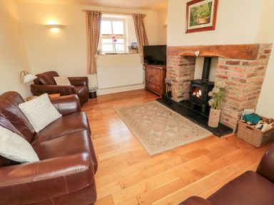A living room with leather sofas a brick fireplace with a wood stove a rug and wooden floor at The Granary in Longframlington near Alnwick
