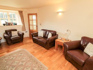 A living room with three brown leather sofas a wooden floor a rug and a wooden door at The Granary in Longframlington near Alnwick