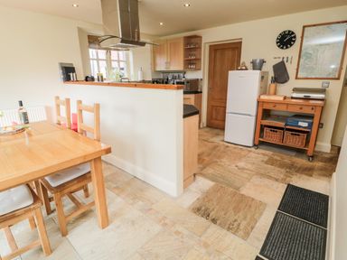 A kitchen with wooden dining table and chairs a refrigerator and a wooden trolley at The Granary in Longframlington near Alnwick