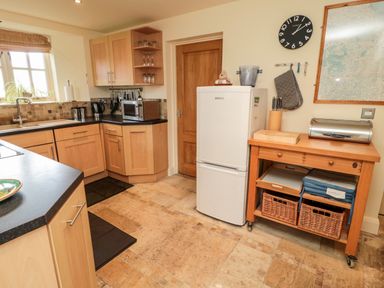 A kitchen with wooden cabinets a refrigerator microwave and a wooden cart with baskets at The Granary in Longframlington near Alnwick