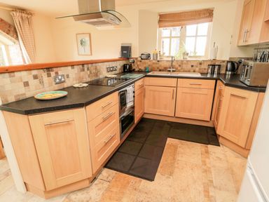 A kitchen with wooden cabinets black countertops a window and appliances at The Granary in Longframlington near Alnwick