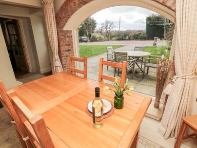 A dining area with a wooden table and chairs a bottle and a vase on the table and a view of an outdoor patio with a round table and chairs at The Granary in Longframlington near Alnwick