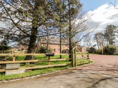 A wooden gate and fence with signs and trees in front of a brick house at The Granary in Longframlington near Alnwick