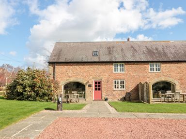 A brick building with a red door and large arched windows with outdoor tables and chairs on grass at The Granary in Longframlington near Alnwick