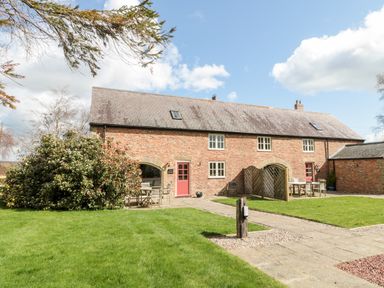 A brick house with red doors and outdoor seating on a lawn at The Granary in Longframlington near Alnwick